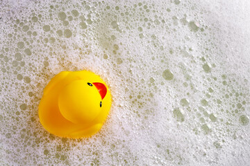 Rubber duck toy floating on water with foam in the bath. Duckling in bubble bathtub with soapy foam.