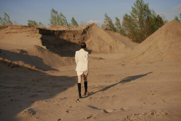 Gorgeous sexy woman walking in the desert. Slim and tan model. Brunette with big lips and long legs. White jacket and skirt, black sunglasses, black boots and turban. Fantastic sand landscape. 