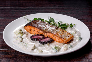 Tasty baked salmon fish on a white dish with broccoli and pea sprouts