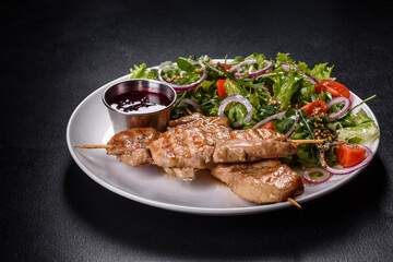Pieces of chicken fillet baked on grilled wooden sticks with salad and red sauce