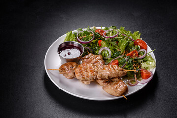 Pieces of chicken fillet baked on grilled wooden sticks with salad and red sauce