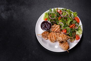 Pieces of chicken fillet baked on grilled wooden sticks with salad and red sauce