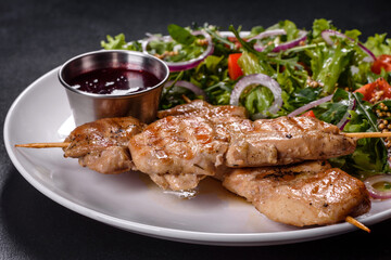 Pieces of chicken fillet baked on grilled wooden sticks with salad and red sauce