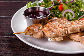 Pieces of chicken fillet baked on grilled wooden sticks with salad and red sauce