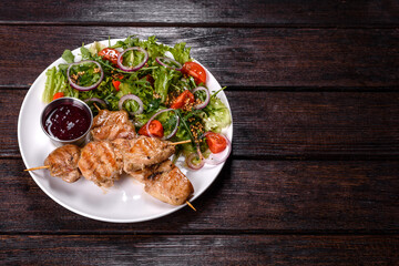 Pieces of chicken fillet baked on grilled wooden sticks with salad and red sauce