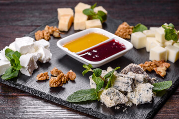 Several types of cheese on a shale tray with mint and sweet sauces