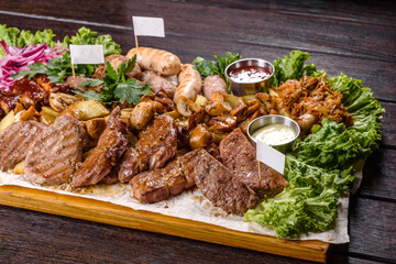 Several types of roasted meat with spices and herbs on a wooden tray