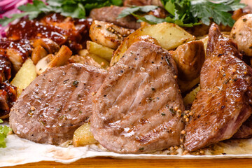 Several types of roasted meat with spices and herbs on a wooden tray