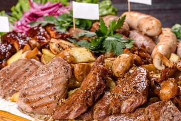 Several types of roasted meat with spices and herbs on a wooden tray