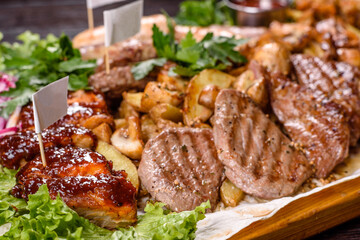 Several types of roasted meat with spices and herbs on a wooden tray