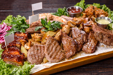 Several types of roasted meat with spices and herbs on a wooden tray