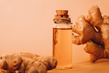 Glass bottle of essential ginger oil, ginger root on beige background. Healthy food eating concept....
