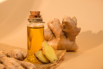 Glass bottle of essential ginger oil, ginger root on beige background. Healthy food eating concept....