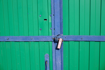 Green corrugated gates in the garage. Blue metal frame with a lock through the shackles