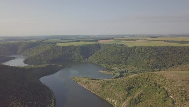 The drone flies over the river. Around the river canyon, which is covered with grass and trees. Morning sun. Dawn. Summer. Gray blue sky. There are no people in the video. Reserve.