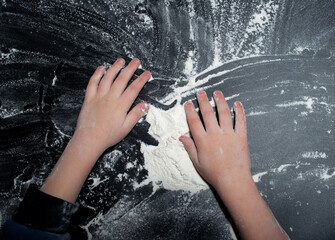 Baby hands on a black background, white powder and flour