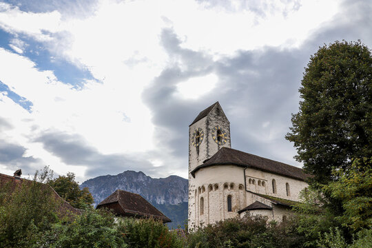 Kirche Amsolldingen, altes Geb&auml;ude, vor Bergkette, bew&ouml;lkter Himmel, Kirchenturm, Scheune, mit b&auml;umen