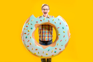 A cute boy is holding a huge donut in his hands, trying to bite him. Cheerful teenager. Confectionery. Delicious dessert. A guy with a funny face