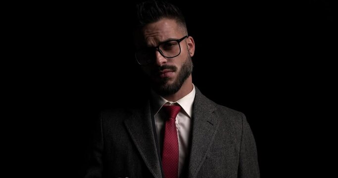young businessman looking at the camera with attitude, arranging his eyeglasses and coat