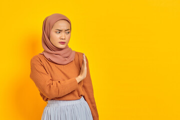 Beautiful annoyed asian woman in brown sweater and hijab makes stop gesture, demonstrates rejection isolated over yellow background. people religious lifestyle concept