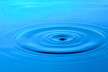 Bright blue background with diverging circles from dropped drop on surface water.