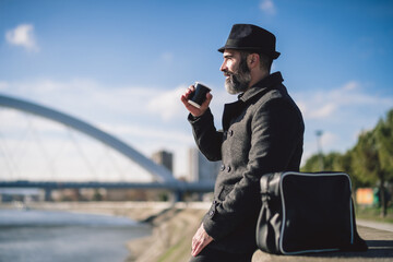 Happy businessman is sitting outdoor in the city and enjoying sun in autumn. He is drinking coffee to go.