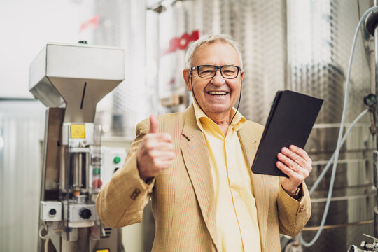 Portrait of happy senior man who owns winery. He is standing beside wine storage tanks and examining cooling process. - Powered by Adobe