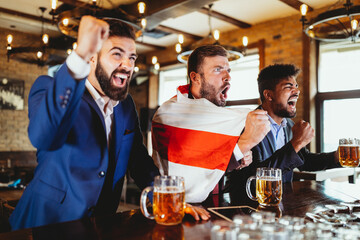 Group of friends at the pub watcing football game and drinking beer