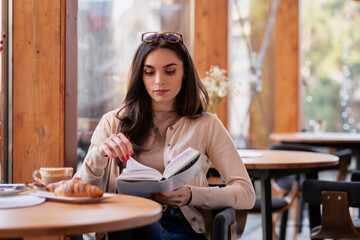 Beautiful young woman reading a book while sitting at the cafe