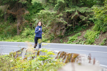 Young fitness woman running on the road through the forest. Slim girl jogging in the morning along the road.