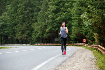 Runner woman running on the mountain road through the forest. Female sport girl training outdoors for marathon