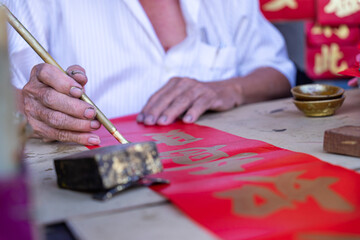 People write Spring Festival couplets with brushes to celebrate Chinese New Year. Chinese New Year scroll with gold ingot and paintbrush. Chinese text translation: Happiness, lucky and wealth.