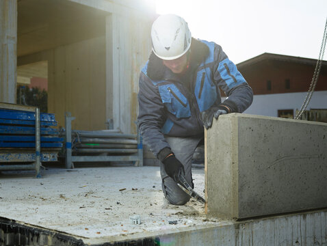Worker cleaning corner of cement slab with hammer kneeling at construction site