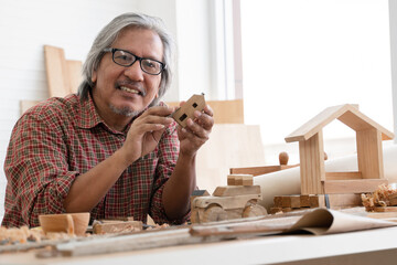 Asian white haired senior carpenter man smiling and using sandpaper to smooth the wooden model....