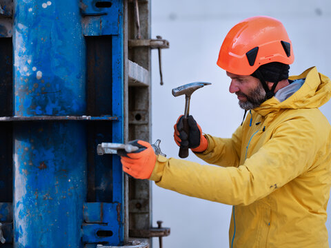 Worker fastening nail on metal structure with hammer