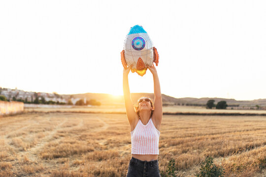 Young woman holding aloft back lit artificial rocket balloon at sunset