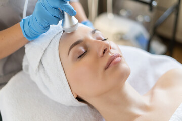 Young woman lying on cosmetologist's table during rejuvenation procedure. Cosmetologist take care...