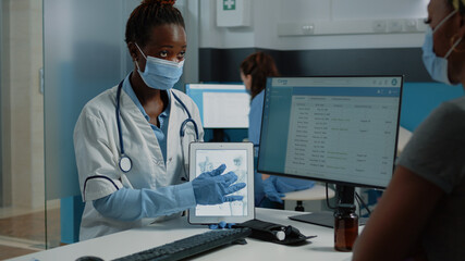 Medic explaining bones fracture to patient for osteopathy examination and wearing face mask in...