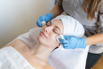 Naklejka premium A young beautiful girl lies on the table at the beautician and receives facial cleansing procedures, makeup removal with white wipes
