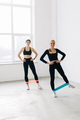 Smiling two women are training with latex band in gym.