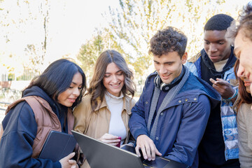 Smiling multiracial students discussing on laptop on university campus