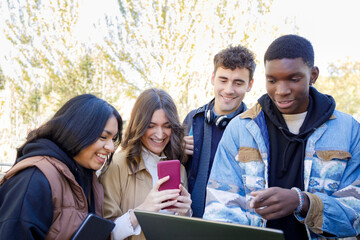Cheerful students with smart phone and laptop on campus