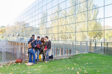 Multiracial students studying together on laptop by college building