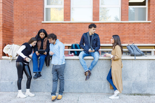 Multiracial students discussing on project by wall on campus