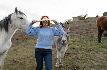 Woman covering eyes with scallions by horse and donkey in ranch