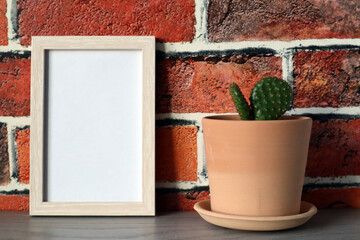 Mock up white frame with clay flower pot with cactus on brick wall background.