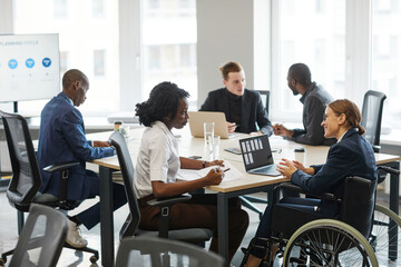 Portrait of successful businesswoman using wheelchair while speaking to employee in meeting, copy space