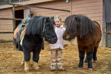 Girl and pony. Child and horses on the farm in the paddock. Equestrian school. Hippotherapy at the...