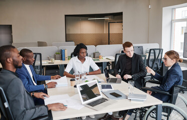 Diverse group of professional business people at meeting table in office with woman using wheelchair