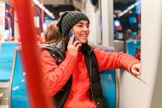 Happy young woman talking on phone and looking out through tram window